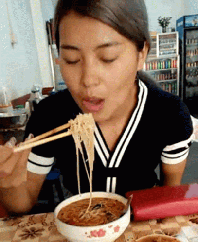 a young woman holding chopsticks eating noodles at a table