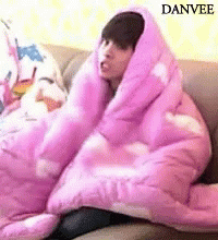 a boy with a jacket on sitting under a pink blanket