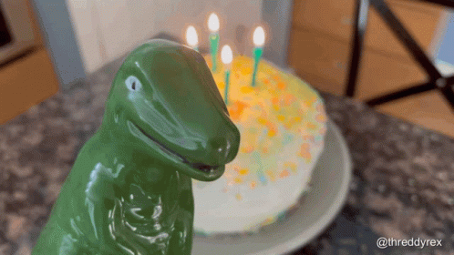 green plastic dinosaur statue sitting in front of cake