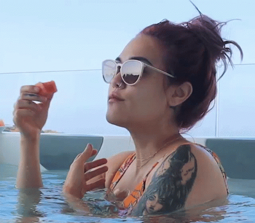 a woman wearing sunglasses is sitting in the water with her hands on a blue object