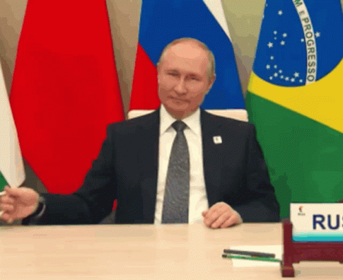two men are sitting at a table with russian flags in the background