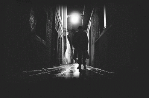 man in black coat with umbrella walking down a dark alleyway