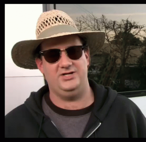 a man wearing sunglasses and a hat standing outside
