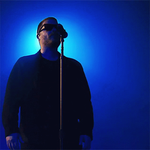 man in black jacket wearing sunglasses singing into a microphone