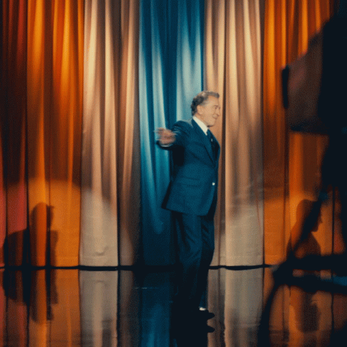 a man in a yellow suit is standing in front of the curtain