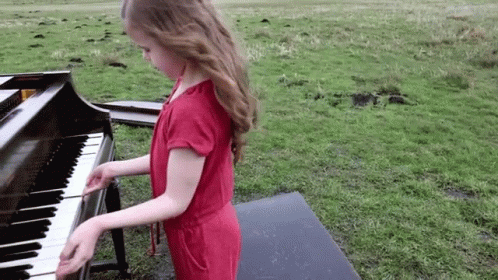 a girl in purple dress playing the piano outdoors