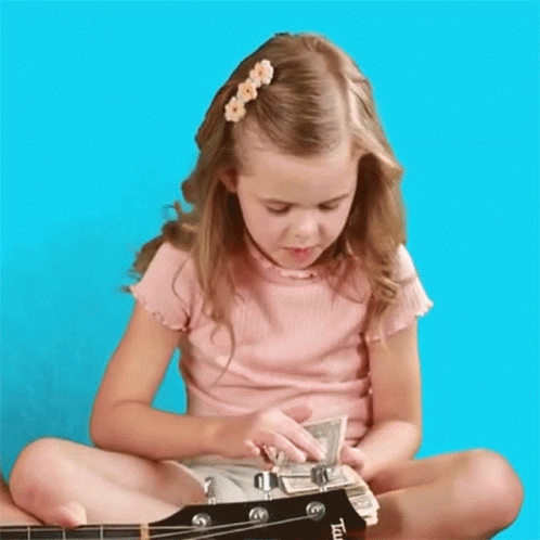 a little girl that is sitting on the ground playing a guitar
