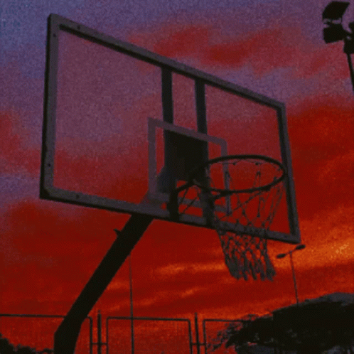 an basketball hoop is lit up against a purple and blue sky