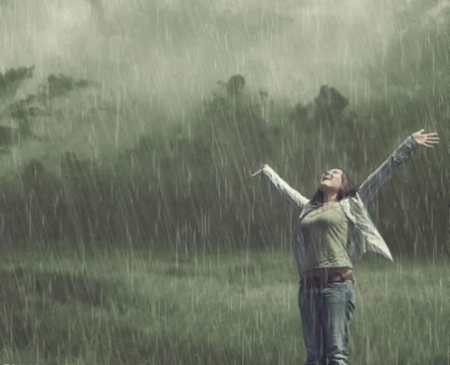 a woman standing in the rain, arms spread up with her hands outstretched