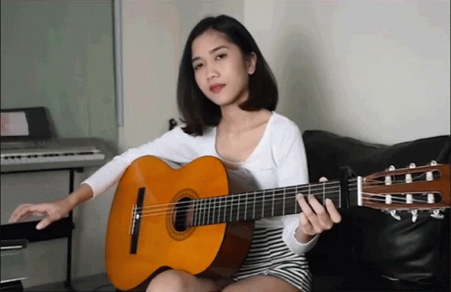 a woman holding an acoustic guitar while sitting on a couch