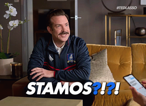 a man with a blue mustache sits in front of an image with a text reading'stamos?? '