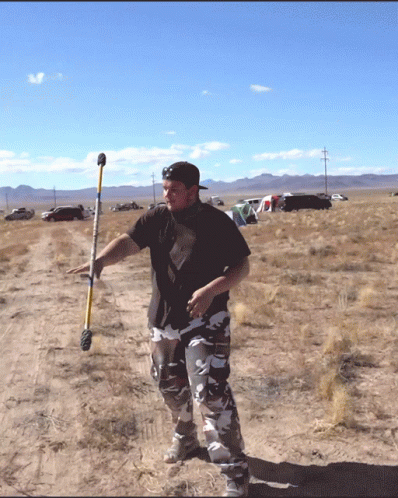 a man holding a metal baseball bat while standing on an empty field