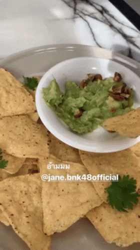 a bowl with blue corn chips and a white plate filled with guacamole
