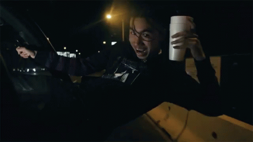 a man sitting in his car holding onto a cup and pointing to the side