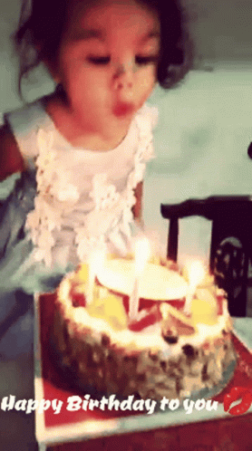 a young child in a white shirt blowing out a birthday candles