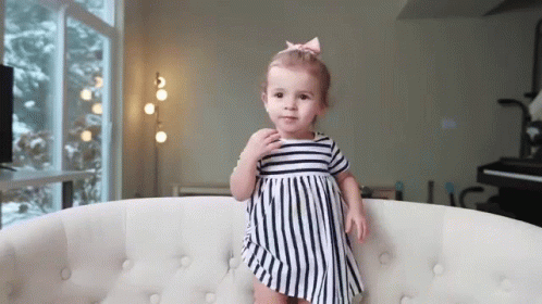 a toddler in a striped dress sits on a white couch