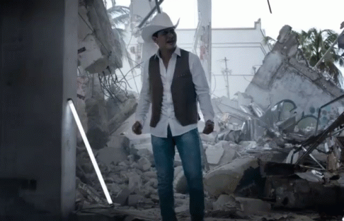 man wearing white hat and vest standing near rubble