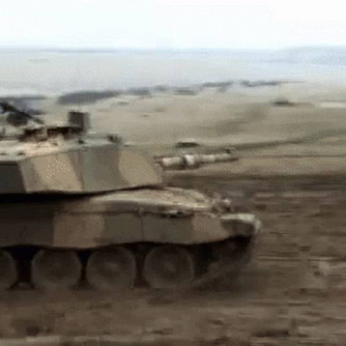 a tank drives through the desert while a smaller tank sits in the foreground