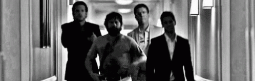 four men stand in an office hallway, looking down at the camera