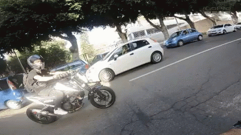 motorcyclist riding in the street with parked cars and parked vehicles behind him