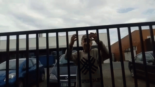 a man covering his eyes and wearing a blue mask behind a metal fence