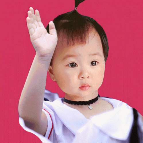 a young asian boy with a very odd head dress holding his hand up