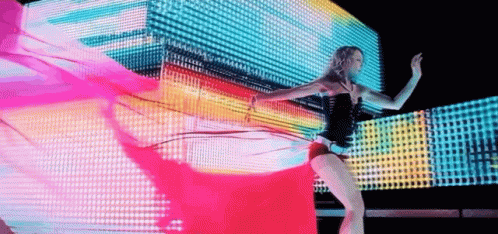 a woman in a black body suit and black heels dancing in front of a group of projected cubes