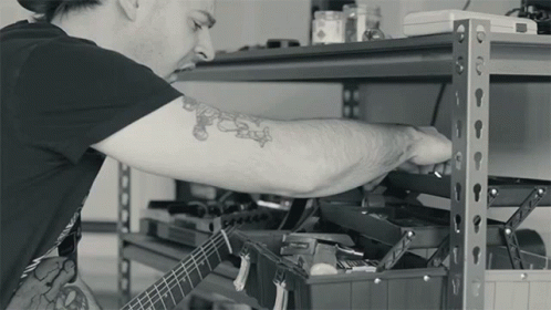 the man has tattoos on his arm as he works on a guitar