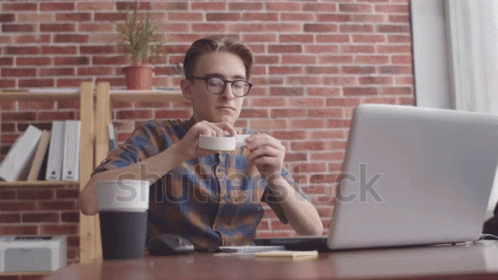 man in plaid shirt drinking a coffee and using his laptop
