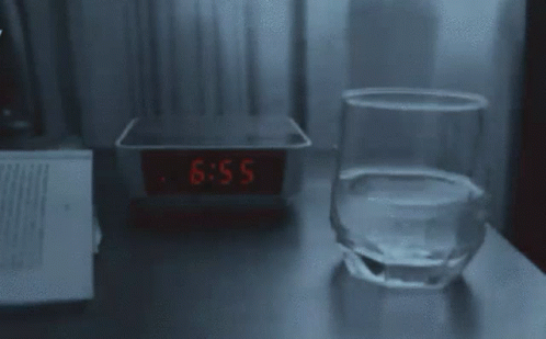 the alarm clock beside an empty glass and a computer on a desk