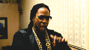 a black man with beads and sunglasses holding up a finger