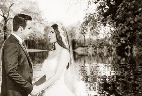 a bride and groom standing on the edge of the lake