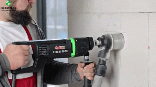 a man is holding a drill and drilling a wall