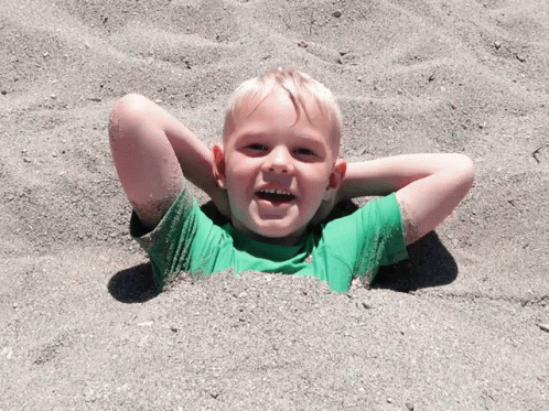 the boy smiles while sitting in the sand