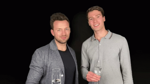 two men standing next to each other with wine glasses in hand