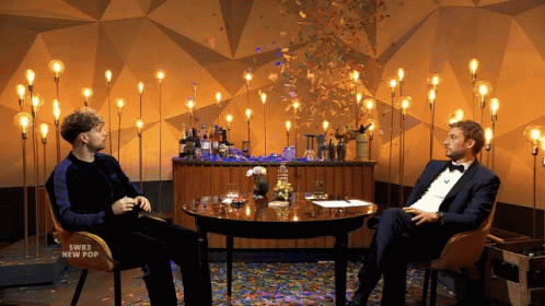 two men sitting at a table with blue lights and a christmas tree