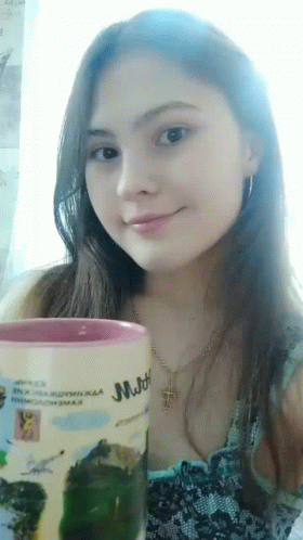 a girl holding a mug sits by a window
