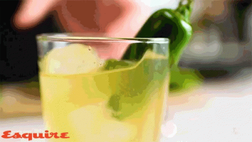 a blue beverage in a glass with a lime and green chilli pepper