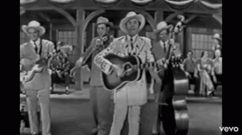 two men in cowboy suits play guitars outside