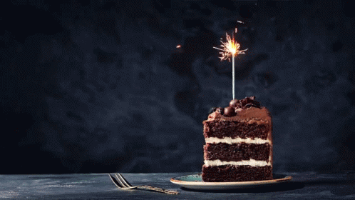a slice of birthday cake with a single lit sparkler on top
