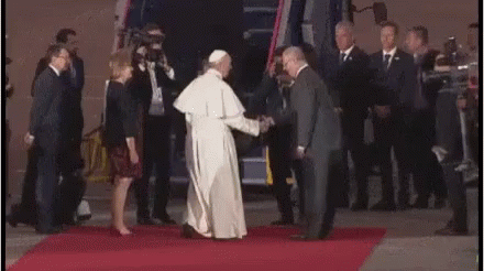 pope walking down a purple carpet with people and camera equipment around