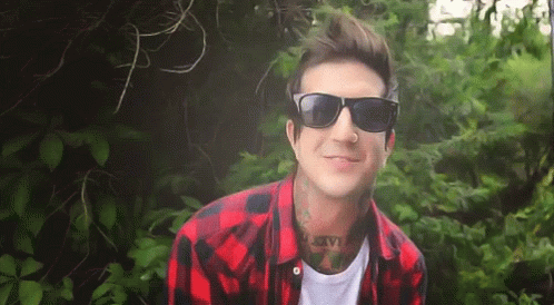 a man in sunglasses, shirt and a plaid shirt with trees around