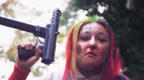 a woman with blue hair and purple makeup holding a gun