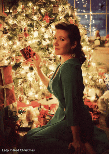 a woman in a green dress sitting by a christmas tree