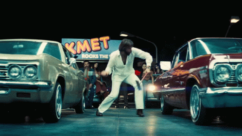 a man in white jacket dancing in front of a line of cars