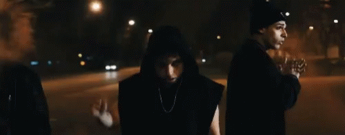 three hooded people walking down a dark street at night