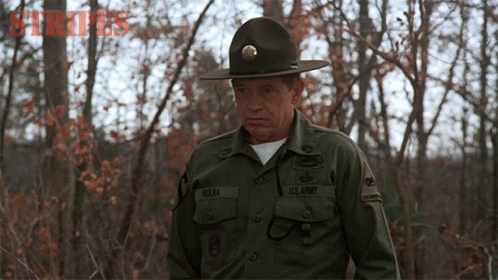 a man with dark makeup and a army uniform standing near a bunch of trees
