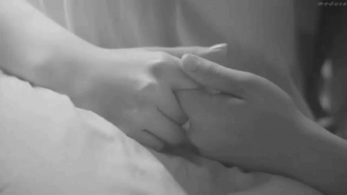 a person holds the hand of another persons in bed