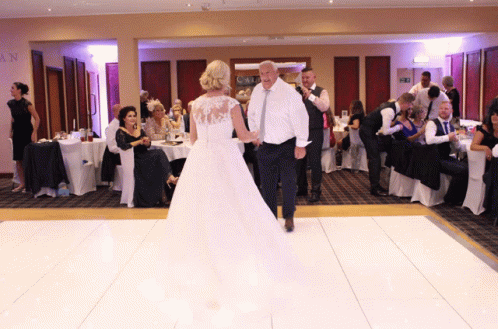 two people dressed up in white are walking on a dance floor