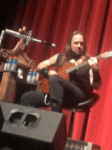 a man playing guitar sitting in a chair on a stage